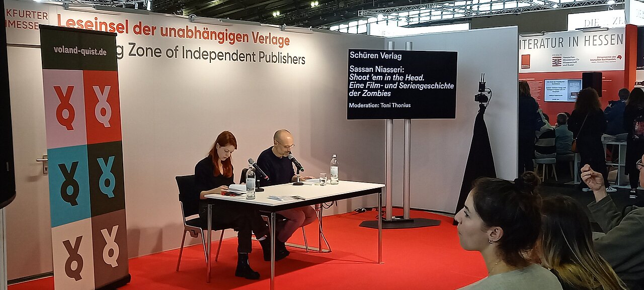 Sassan Niasseri liest auf der Frankfurter Buchmesse (2023). Foto: Niasseri, CC BY-SA 4.0, via Wikimedia Commons; https://upload.wikimedia.org/wikipedia/commons/4/44/Frankfurter_Buchmesse_Shoot_%60em_in_the_Head.jpg