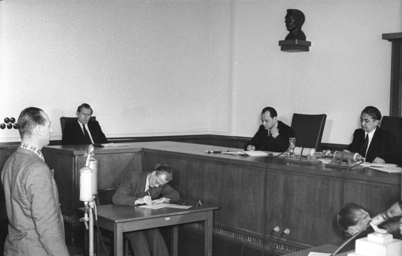 Schwarz-weiß-Foto: Ein Mann spricht stehend vor sitzenden Männern in einem Gerichtssaal.