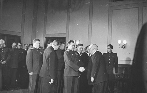 Schwarz-weiß-Foto: Männer in Anzügen stehen eng beieinander. Zwei von ihnen schütteln sich die Hand.