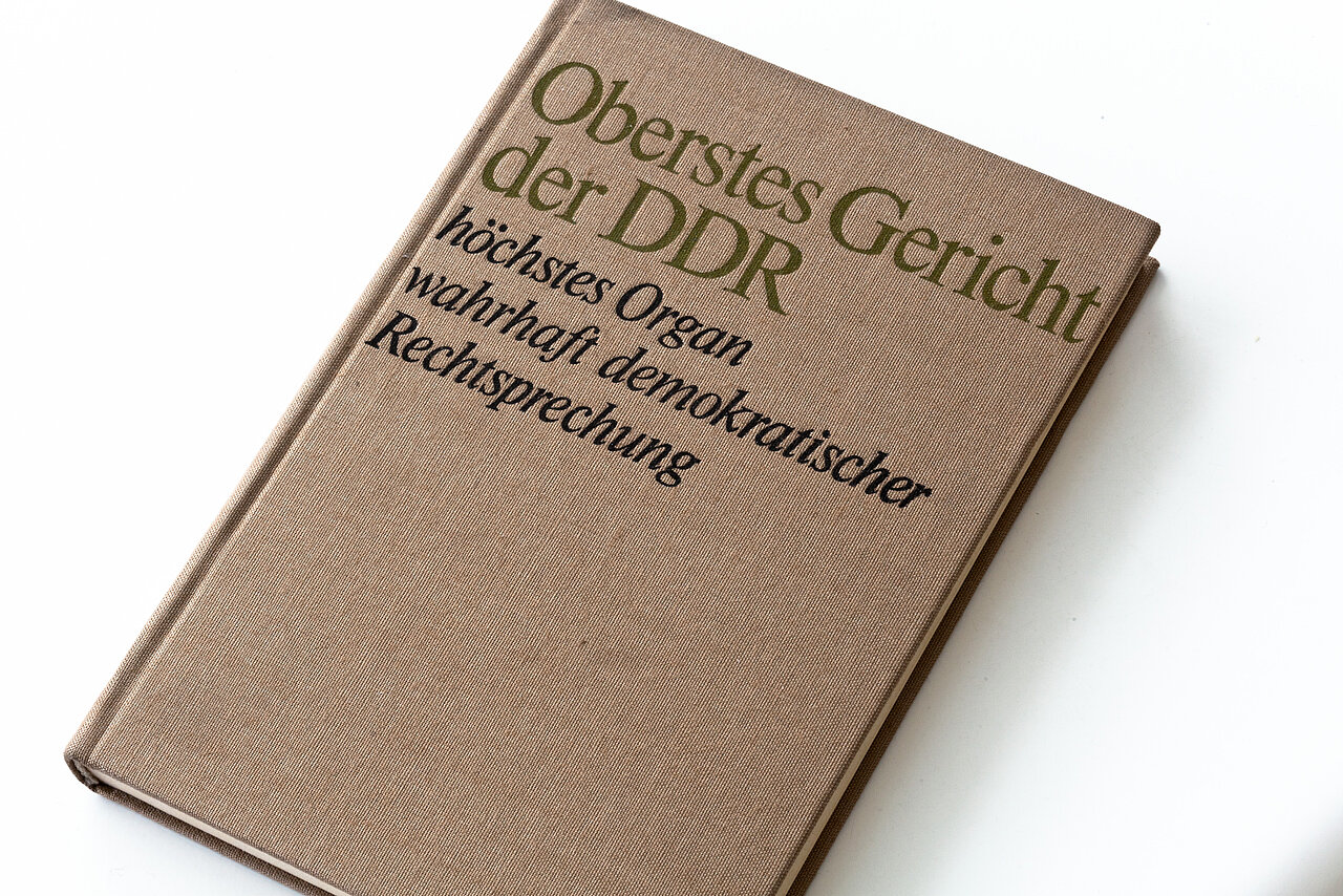 Farbfoto: Braunes Buch mit der Aufschrift: Oberstes Gericht der DDR, höchstes Organ wahrhaft demokratischer Rechtssprechung